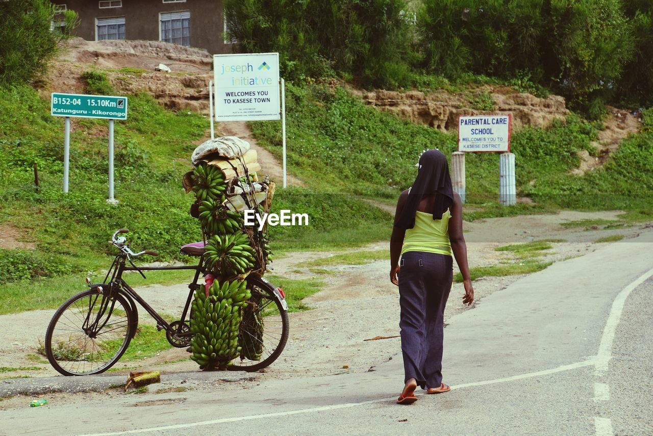 Rear view of woman walking by bicycles with bananas on roadside
