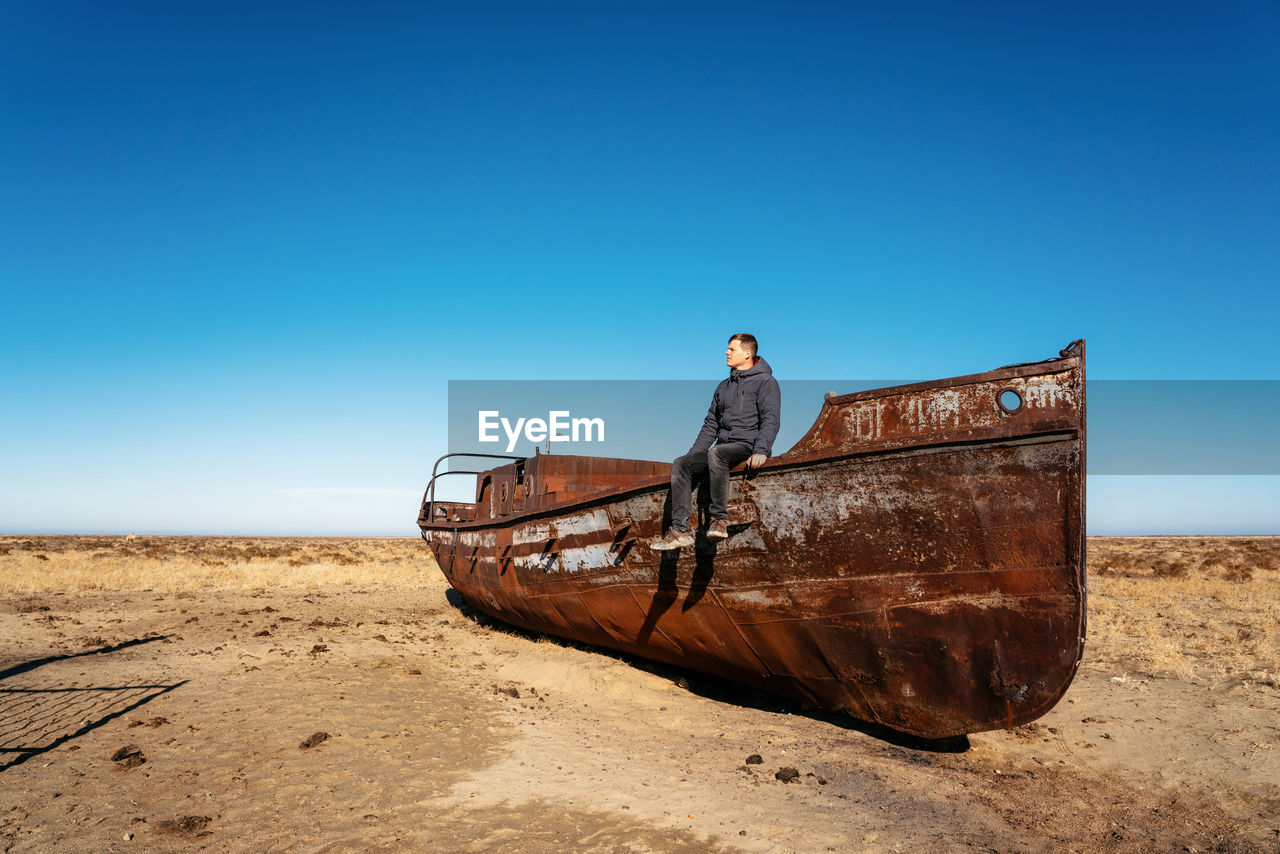 Man on boat at beach against clear blue sky