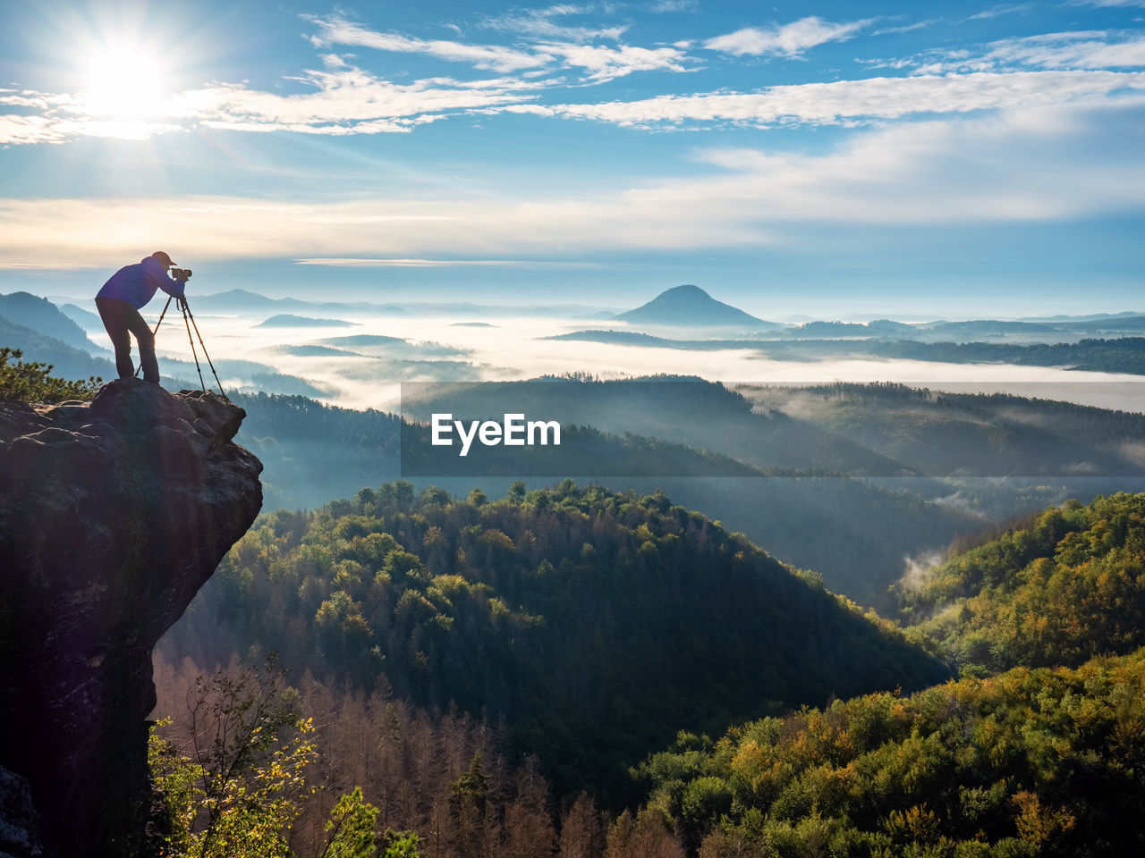 Photographer on mountain witch through viewfinder. morning landscape from top of the mountain