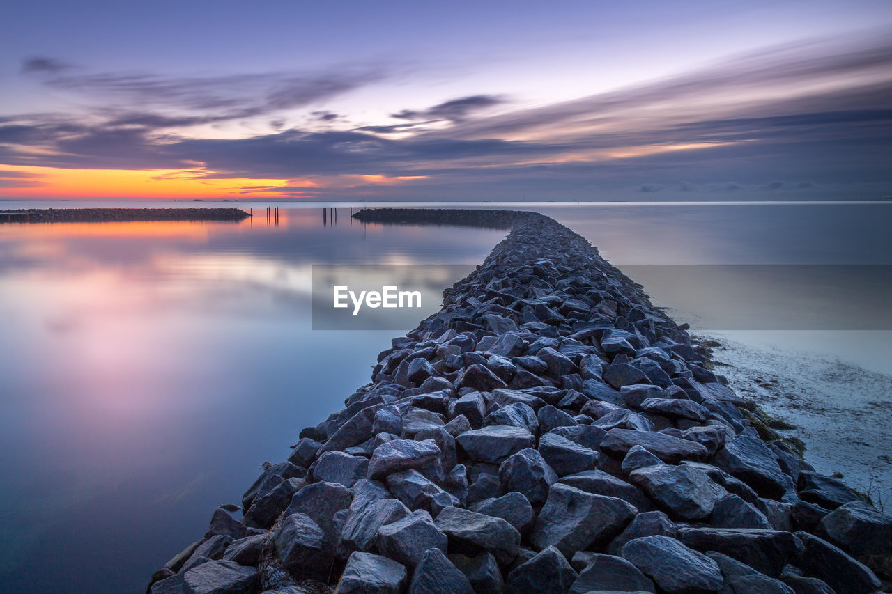 STACK OF ROCKS ON SEA AGAINST SKY DURING SUNSET