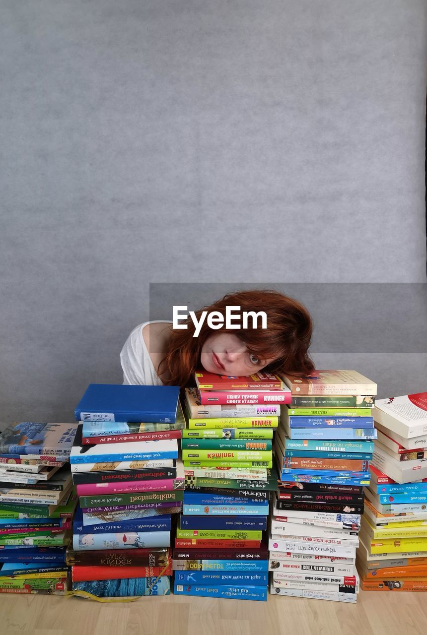 PORTRAIT OF YOUNG WOMAN SITTING BY BOOKS ON SHELF