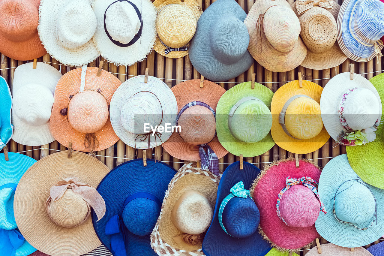 A variety of fashionable and colorful hats hanging on the bamboo backdrop of curbside shop.