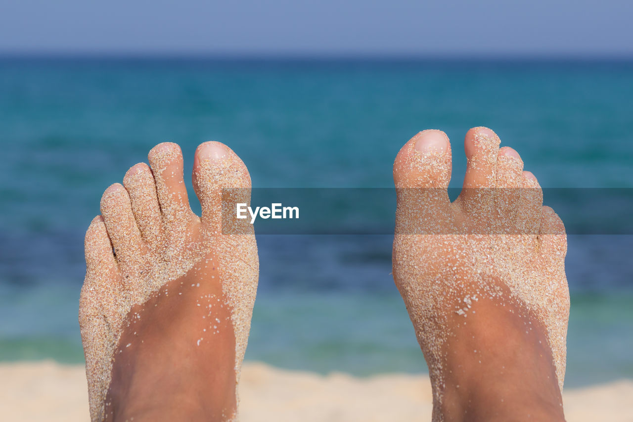 Low section of sandy feet at beach against sea