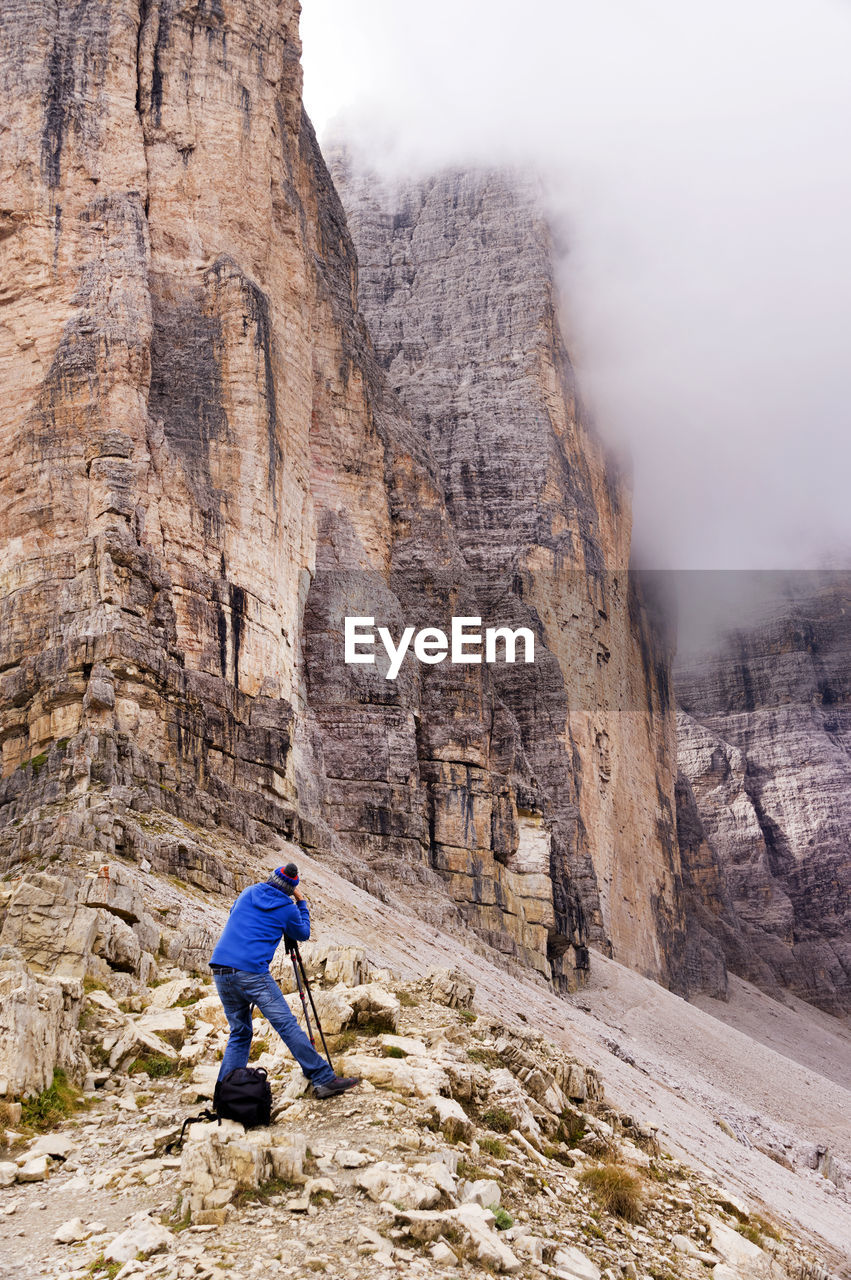 Rear view of man photographing tre cime di lavaredo at dolomites during foggy weather