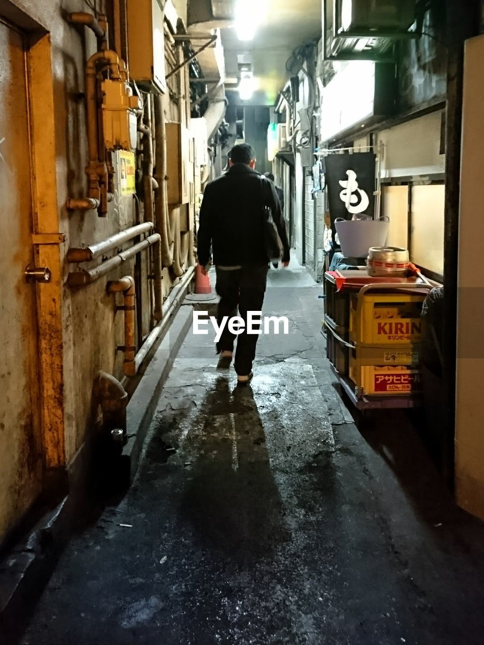 FULL LENGTH REAR VIEW OF MAN WALKING ON ILLUMINATED STREET