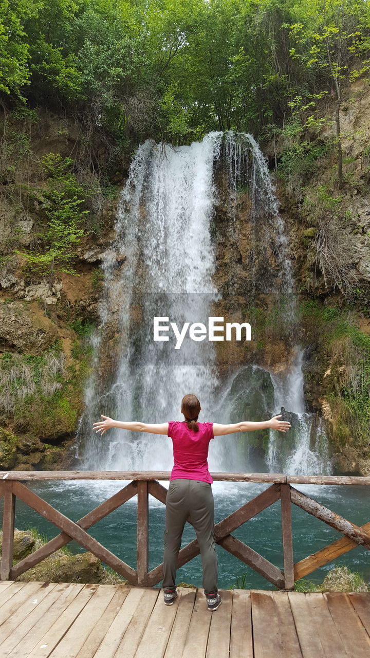 Rear view of woman standing against waterfall