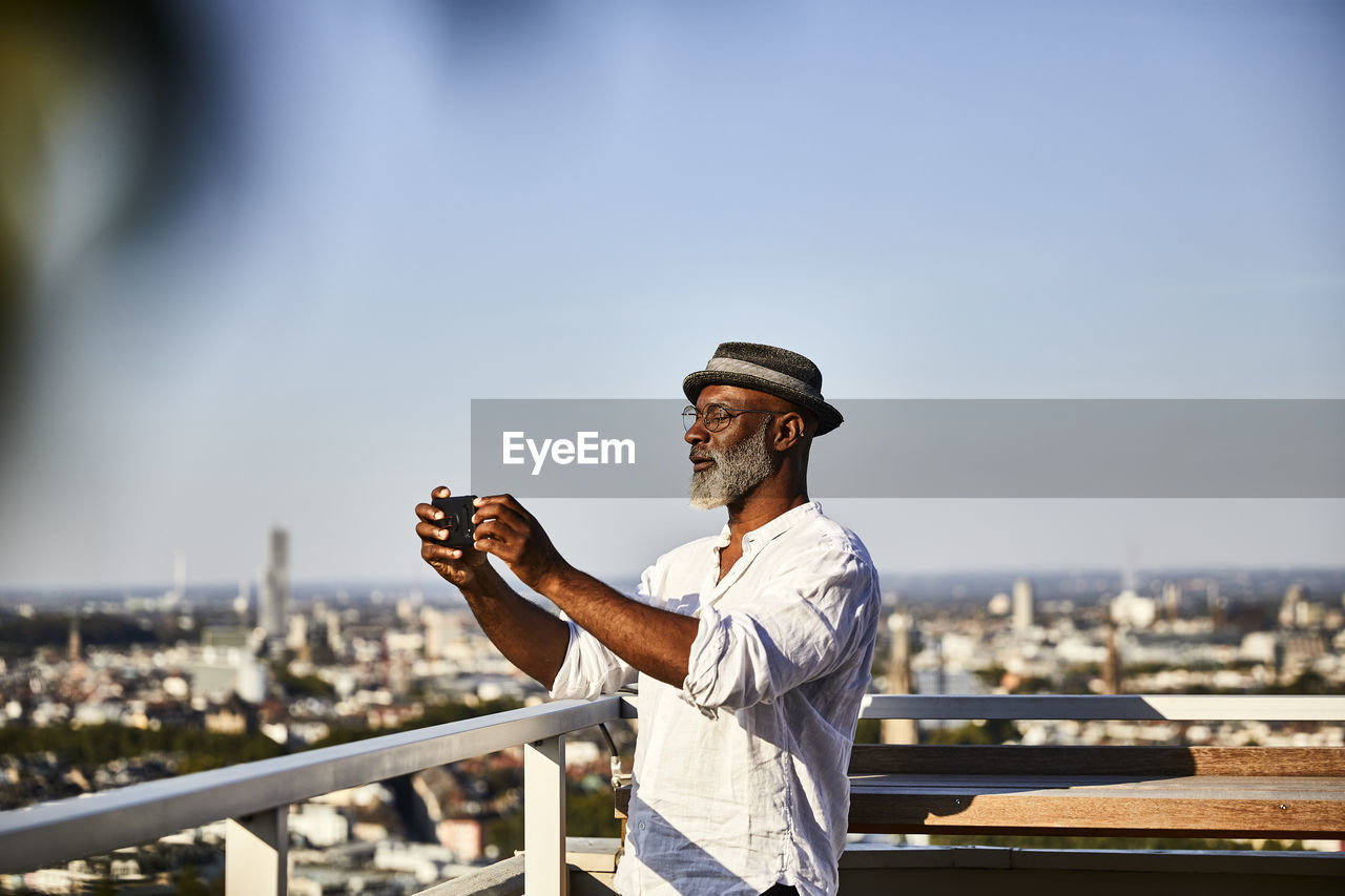 Mature man taking selfie while using smart phone standing on building terrace