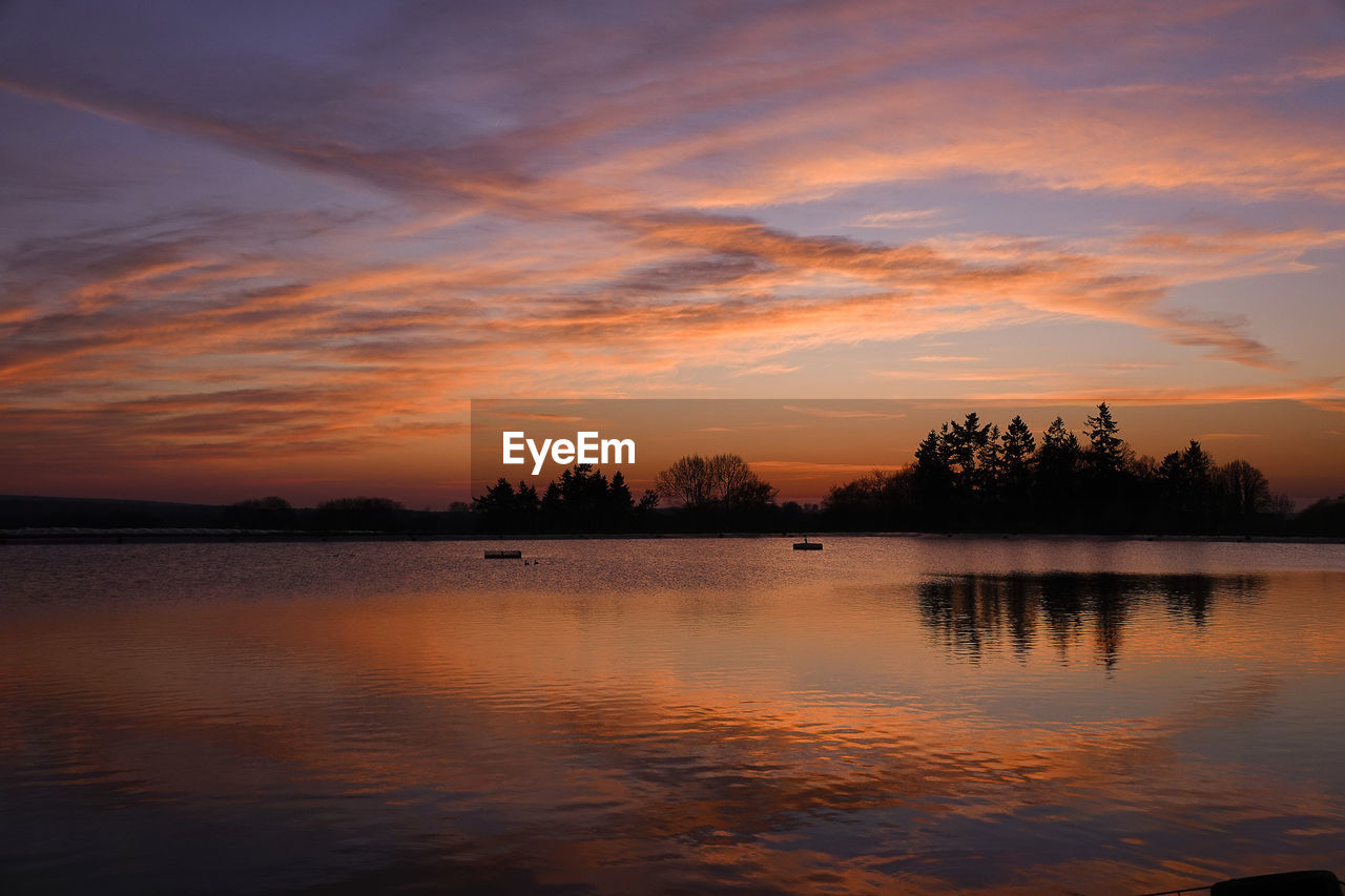 SILHOUETTE TREES BY LAKE AGAINST ORANGE SKY