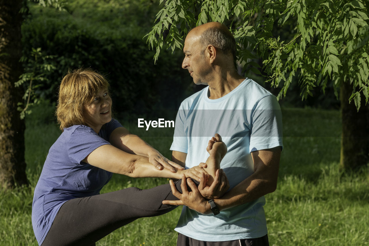 Mature couple stretching legs together while exescising to improve their health in elder ages