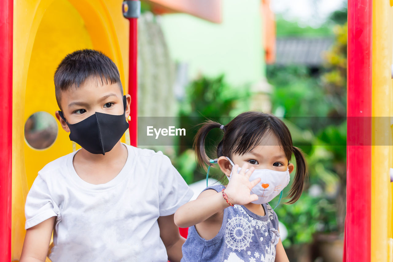 Portrait of siblings wearing masks playing in playground