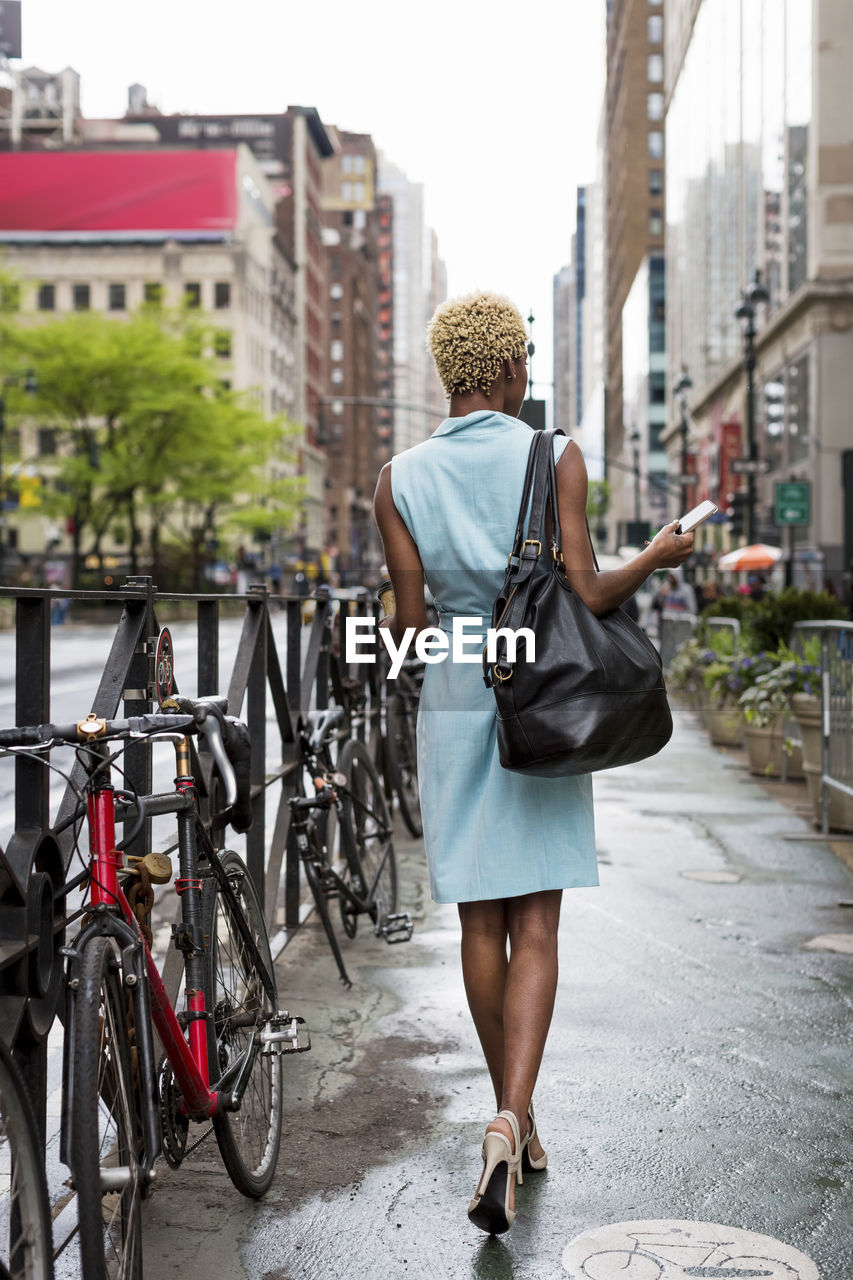 Usa, new york, young blonde african-american woman with smart phone walking on walkway