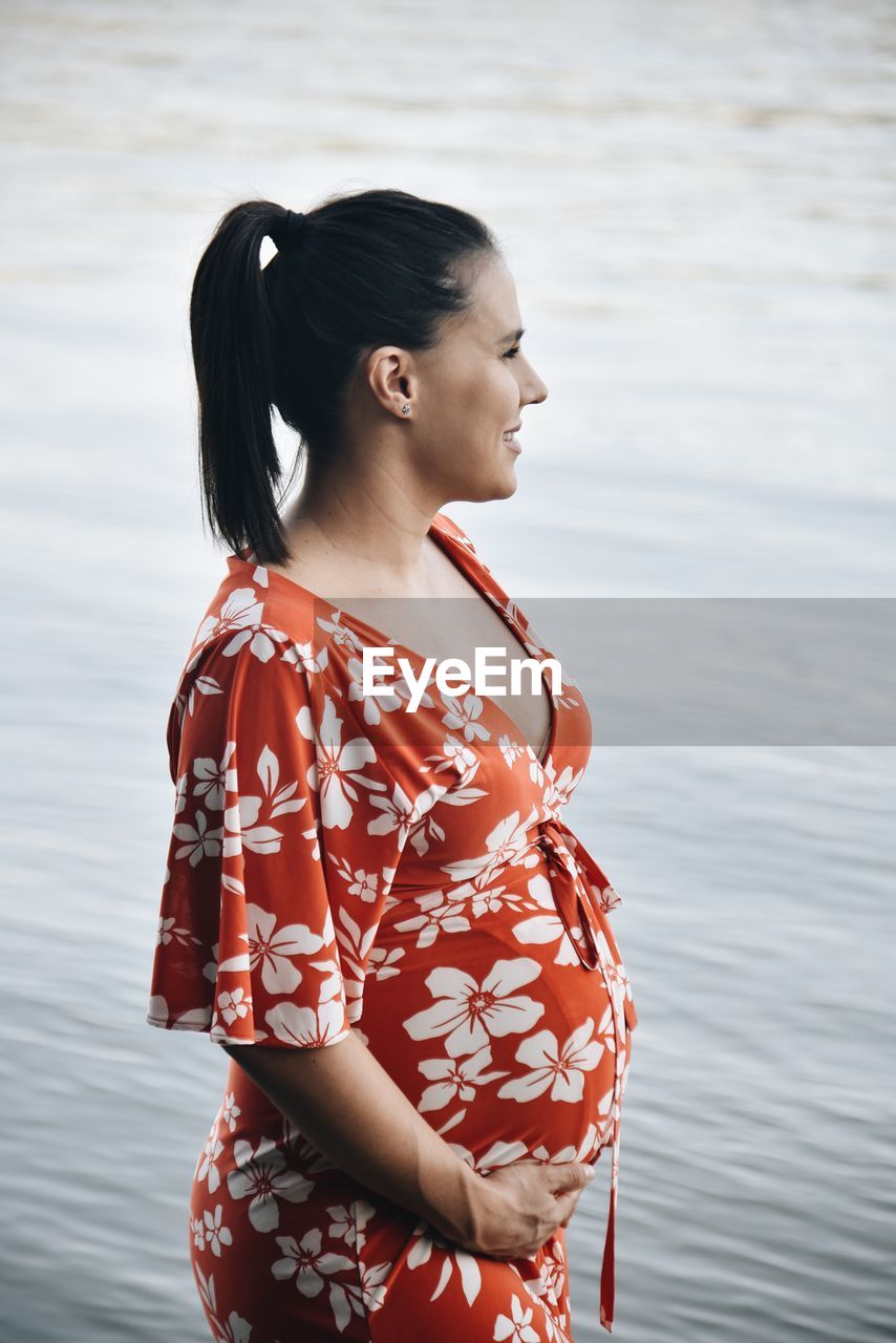 Young pregnant woman looking away while standing in water