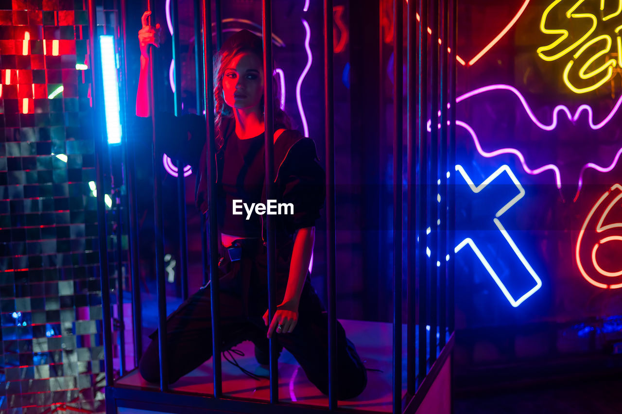 Caucasian woman in a cage in a neon studio