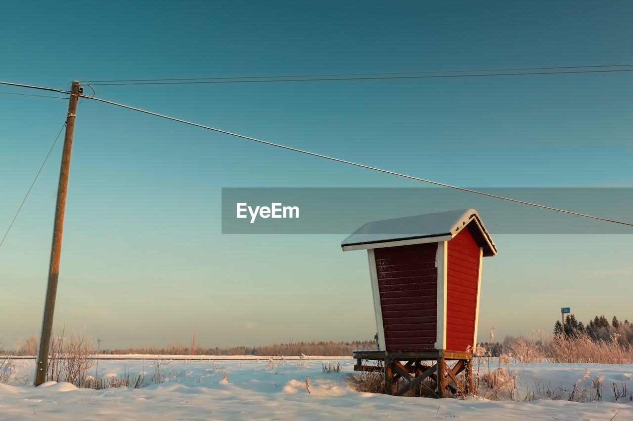 Built structure by telephone pole on snowy field against clear sky