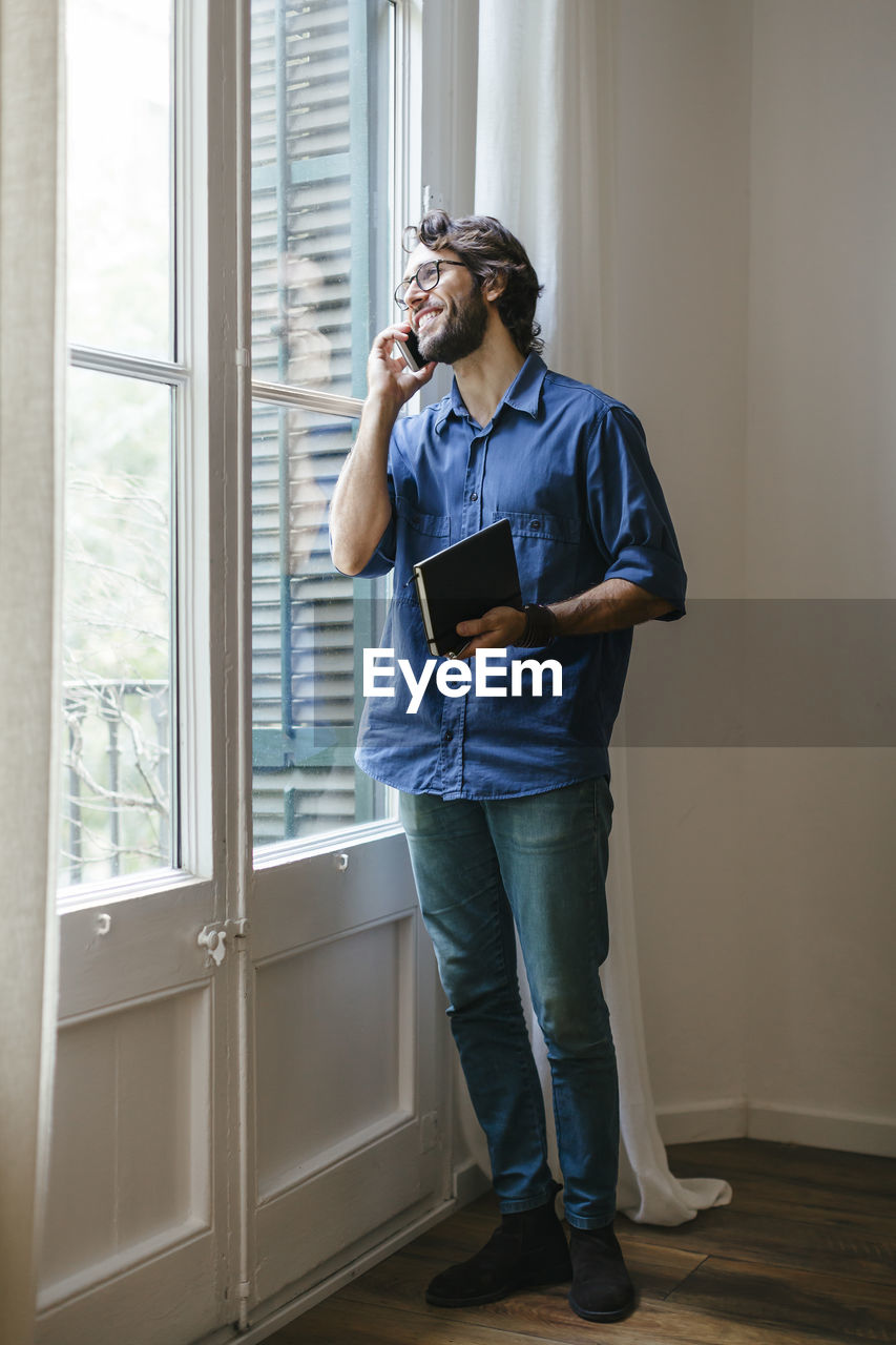 Businessman standing at office window, using smart phone