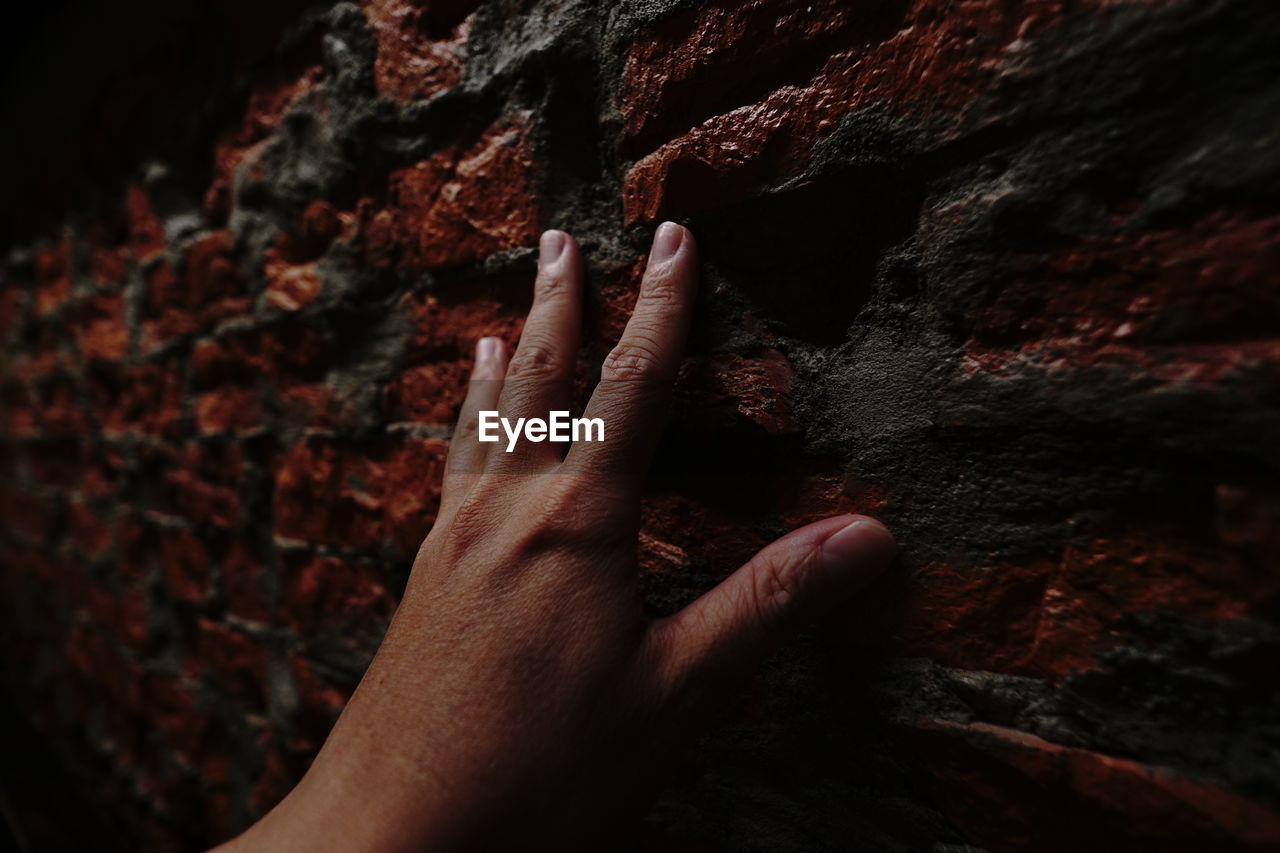 Close-up of hand touching brick wall 