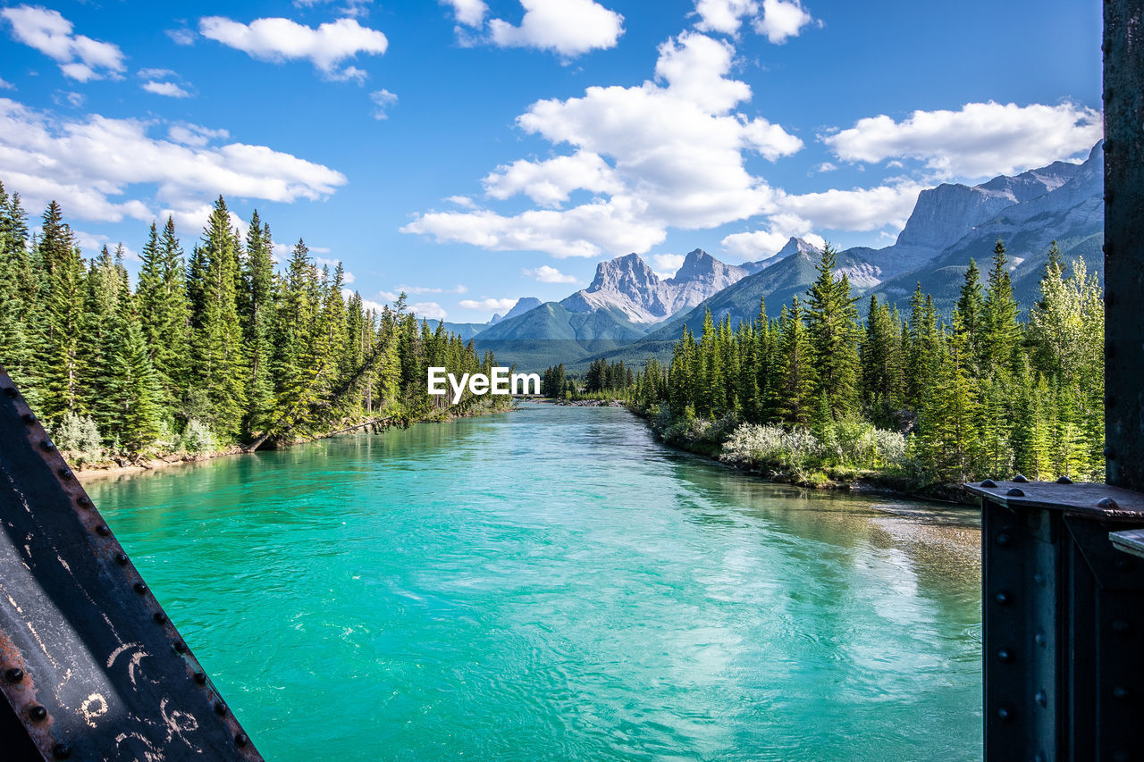 Scenic view from a bridge looking over a river with a forest and mountain setting and blue sky.