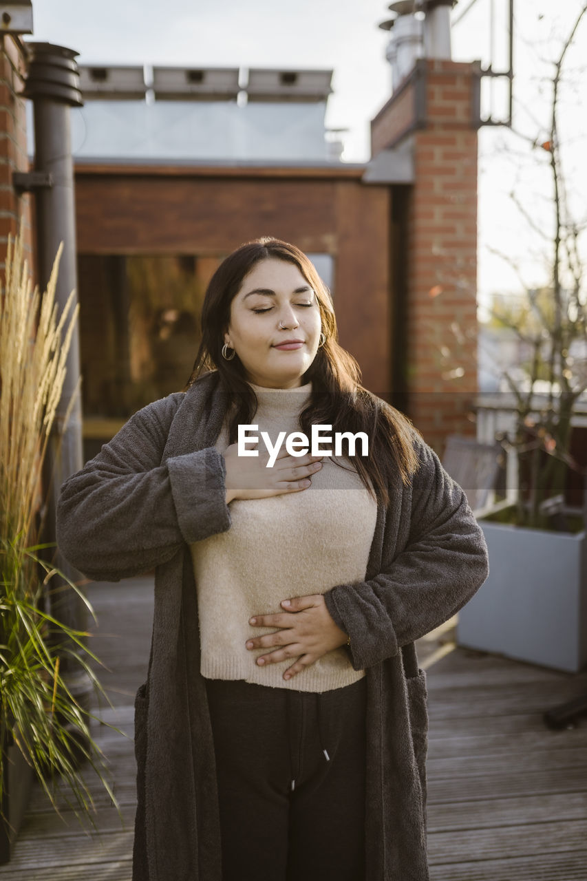 Woman with eyes closed practicing breathing exercise while standing at terrace