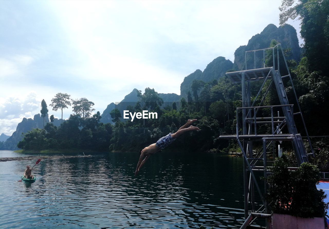 Man jumping in lake against sky