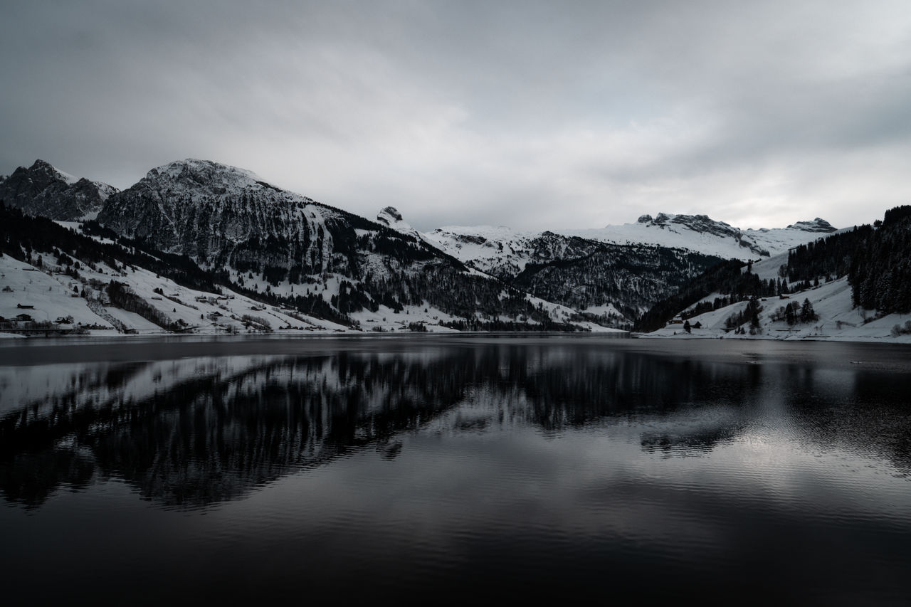 mountain, reflection, scenics - nature, water, nature, snow, lake, beauty in nature, sky, cold temperature, environment, mountain range, winter, landscape, cloud, tranquil scene, tranquility, monochrome, black and white, snowcapped mountain, no people, monochrome photography, tree, travel destinations, morning, land, non-urban scene, forest, outdoors, travel, plant, wilderness, idyllic