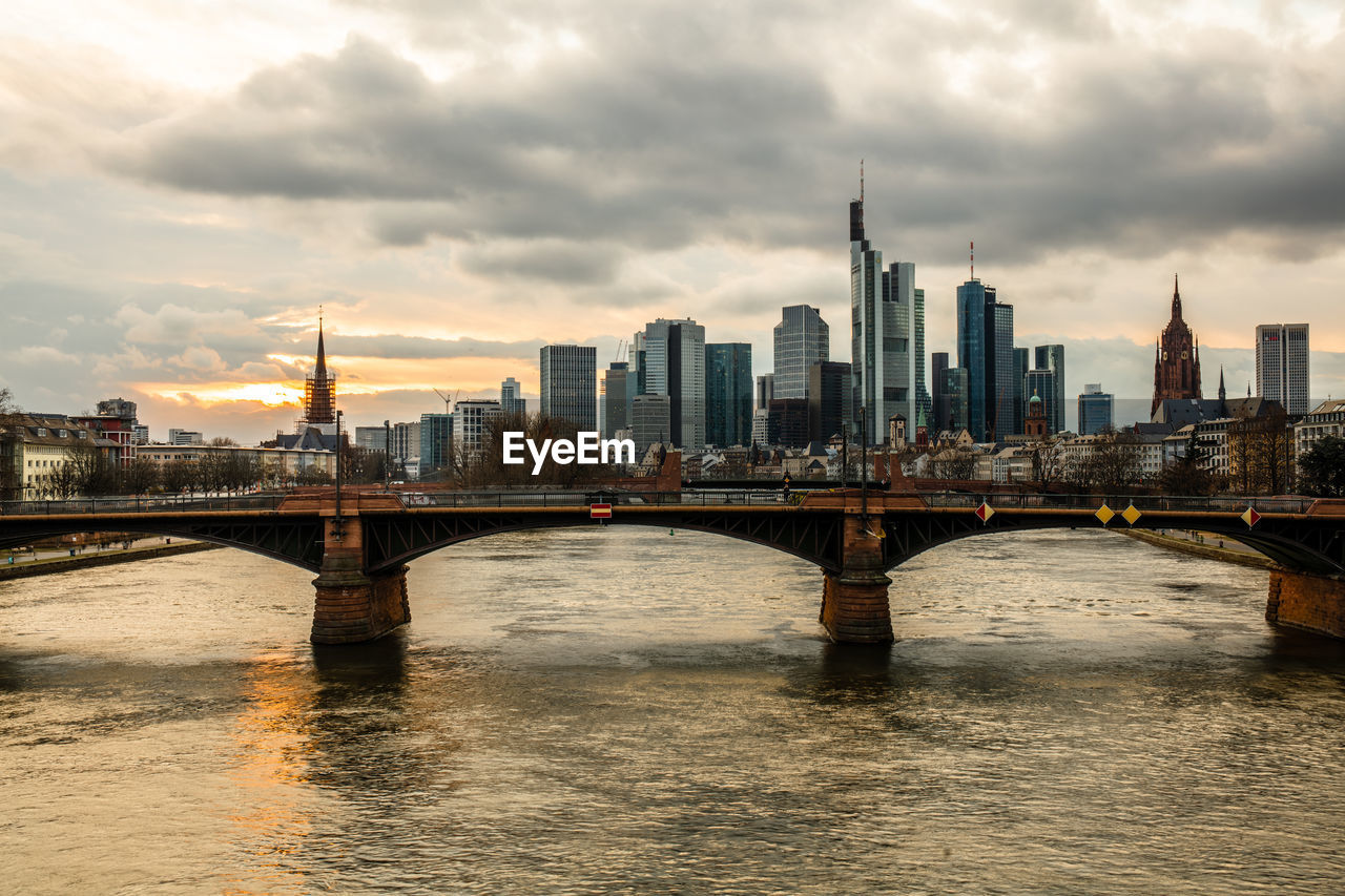 BRIDGE OVER RIVER BY BUILDINGS AGAINST SKY