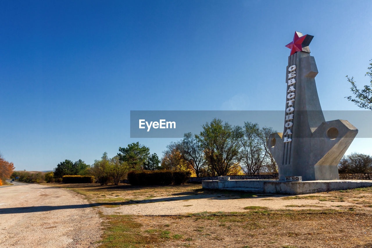 sky, nature, monument, blue, tree, architecture, statue, plant, clear sky, no people, sculpture, sunny, day, tower, landmark, memorial, history, built structure, outdoors, sunlight, the past, travel destinations, flag, copy space