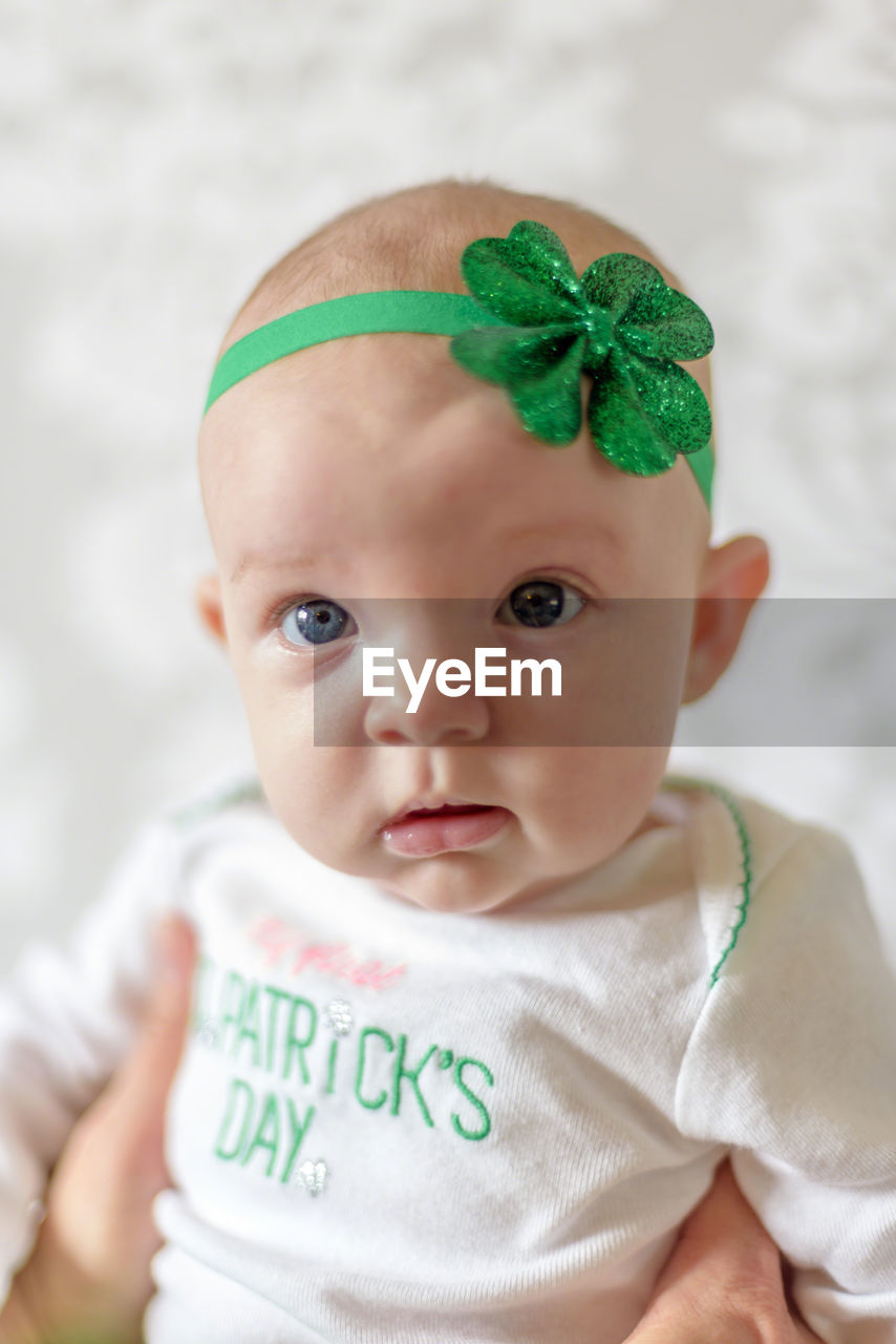 Cropped hand holding cute baby girl wearing green headband