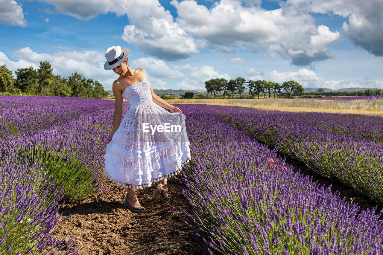Beautiful woman posing in a blooming lavender field with her white dress and hat. 