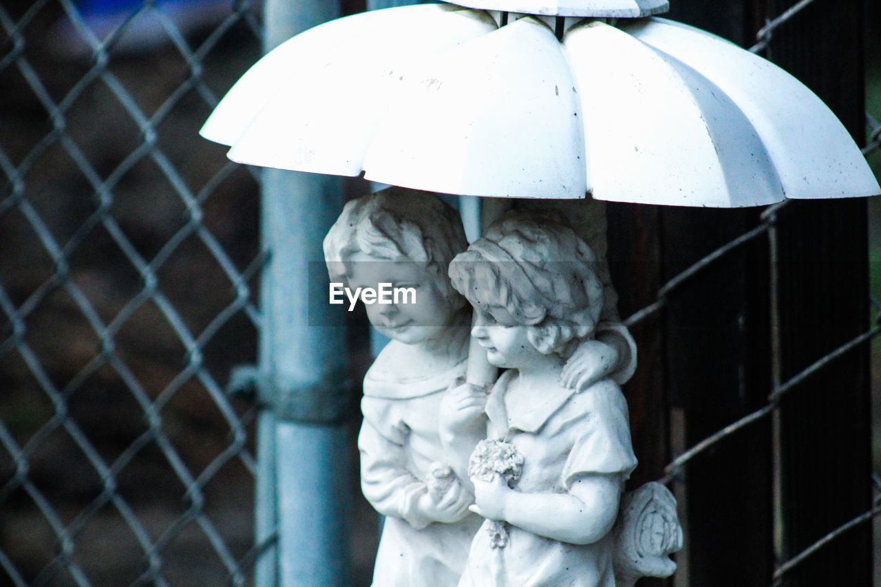 Statue of couple with umbrella by chainlink fence