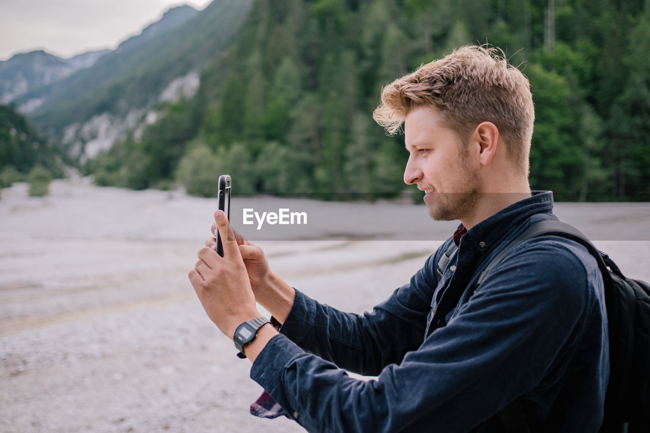 Side view of young man using mobile phone while standing on land