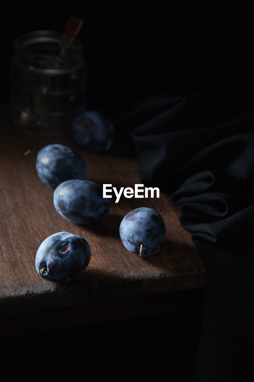 Blue plum on a wooden table against the background of a glass jar