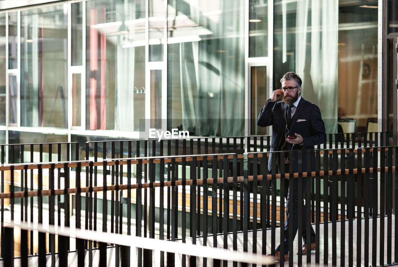 Full length of businessman using smart phone while walking in atrium