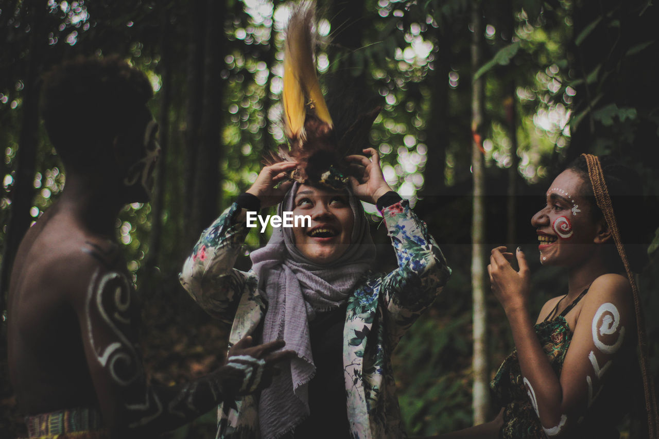 PORTRAIT OF A SMILING YOUNG WOMAN STANDING IN FOREST