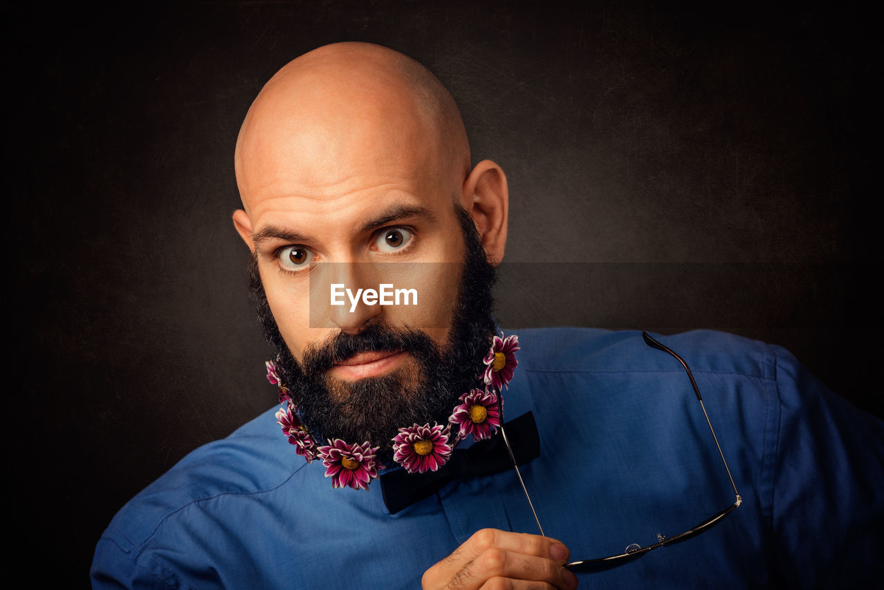 Portrait of hipster with flowers in beard against black background