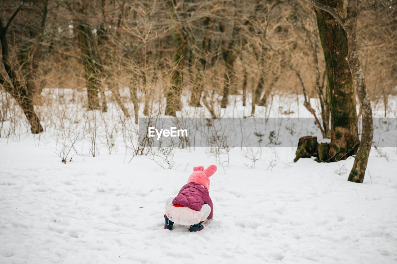 Rear view of girl playing on snowy field against bare trees