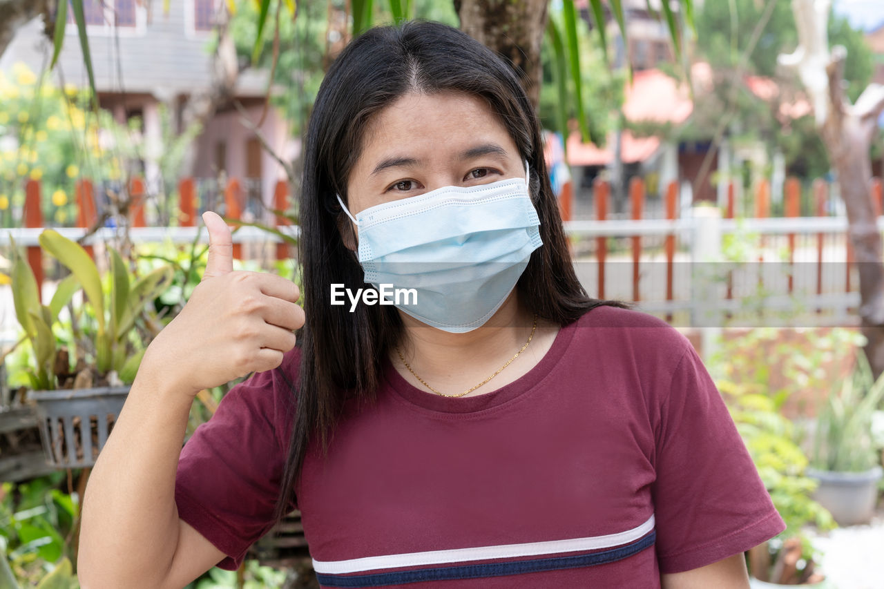 Adult woman wearing medical face mask. pretty middle female showing finger thumb up for good sign.