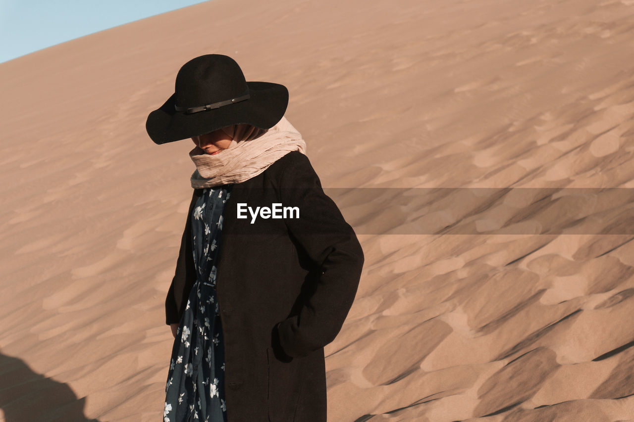 Woman wearing hat standing on sand dunes or desert