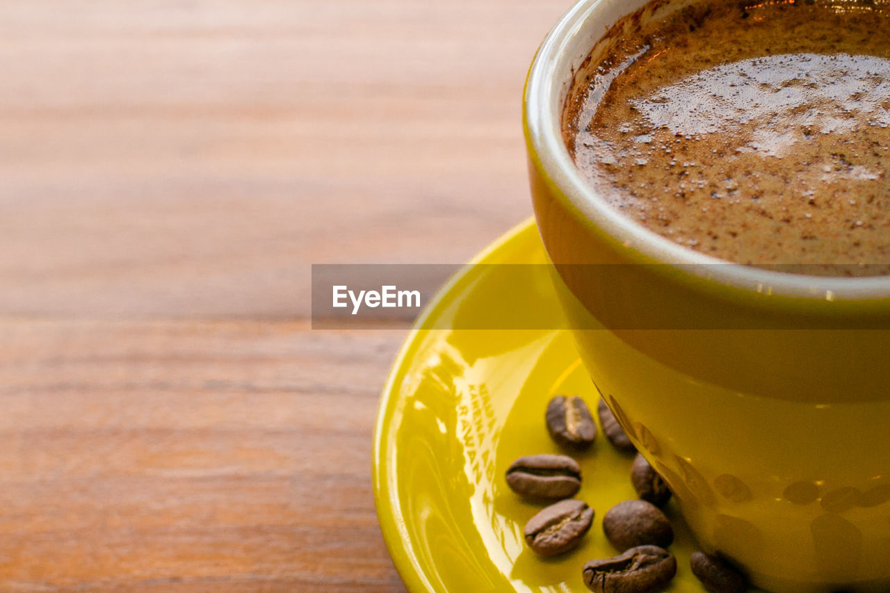 Yellow cup coffee on wood background. roast coffee bean on the yellow plate of coffee