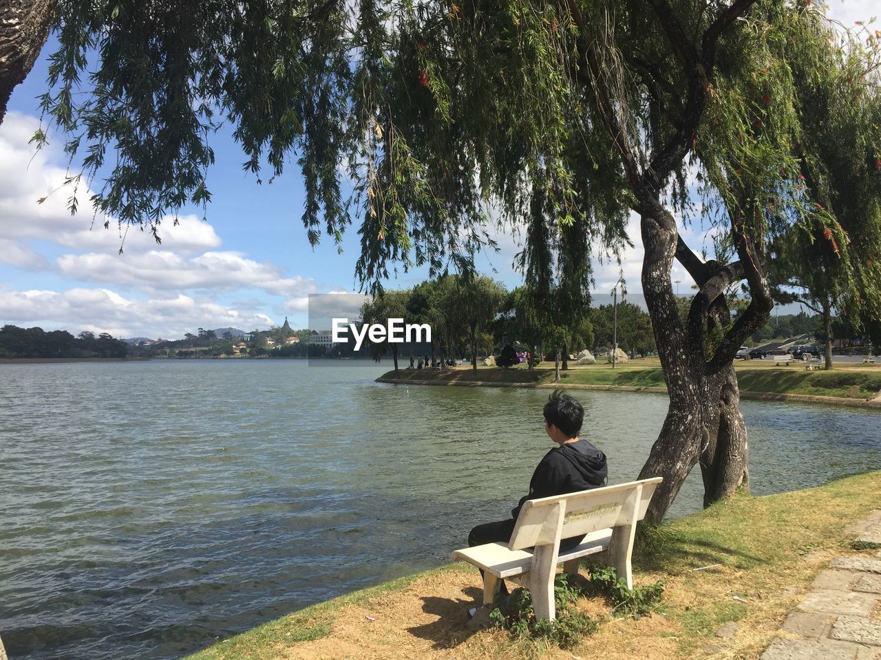 Man sitting on bench by lake against sky
