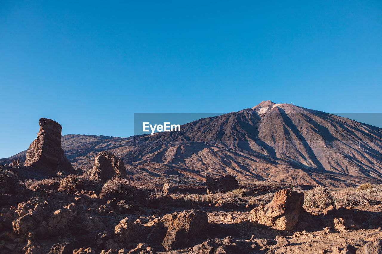 Scenic view of volcanic mountain against clear blue sky