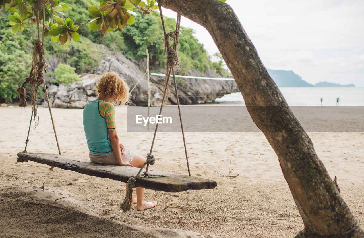 Full length of woman sitting on swing at beach