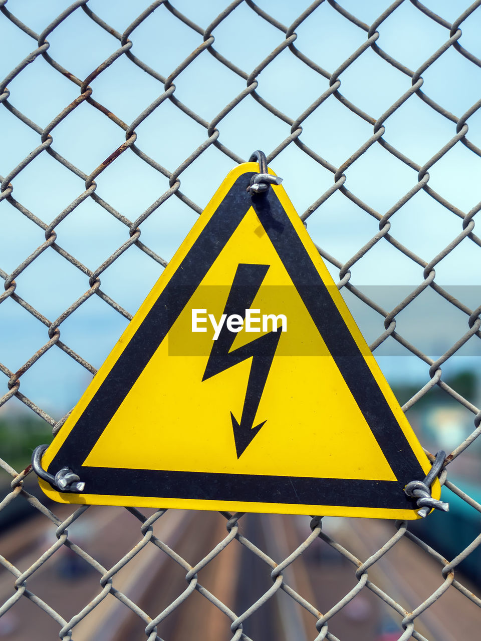 Yellow sign with lightning in triangle. the sign is hanging on the fence of a chain-link netting