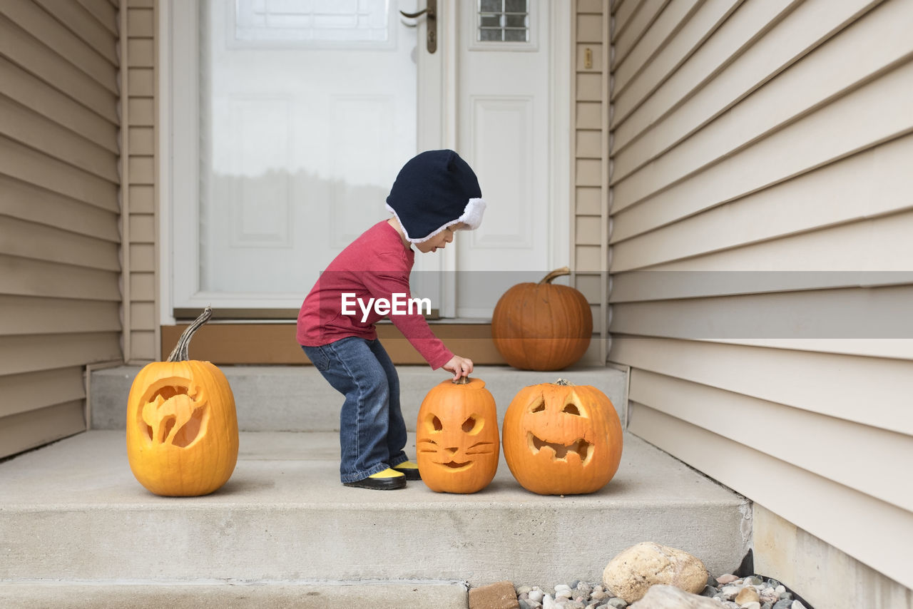 Side view of baby boy holding jack o lantern while standing at entrance