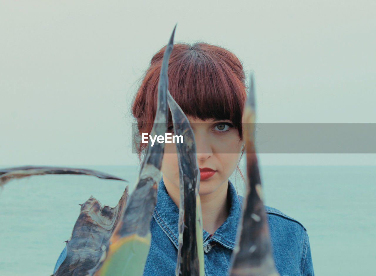 Portrait of woman looking through plants against sea