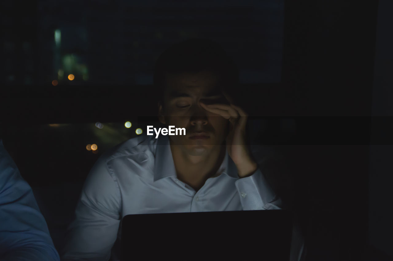 Tired businessman rubbing eyes while working late in office at night