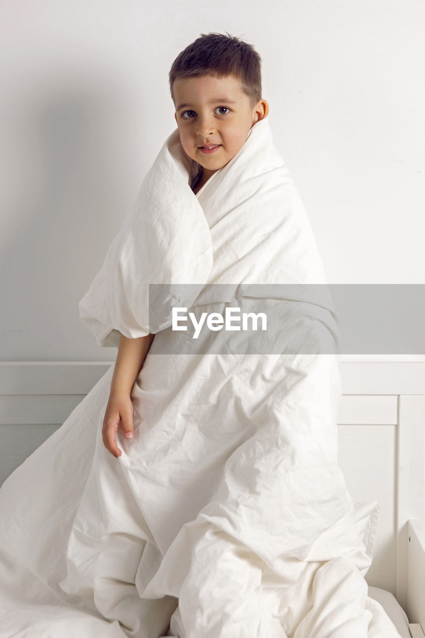 Child boy is mad having fun in a white bed in the children's room with a blanket