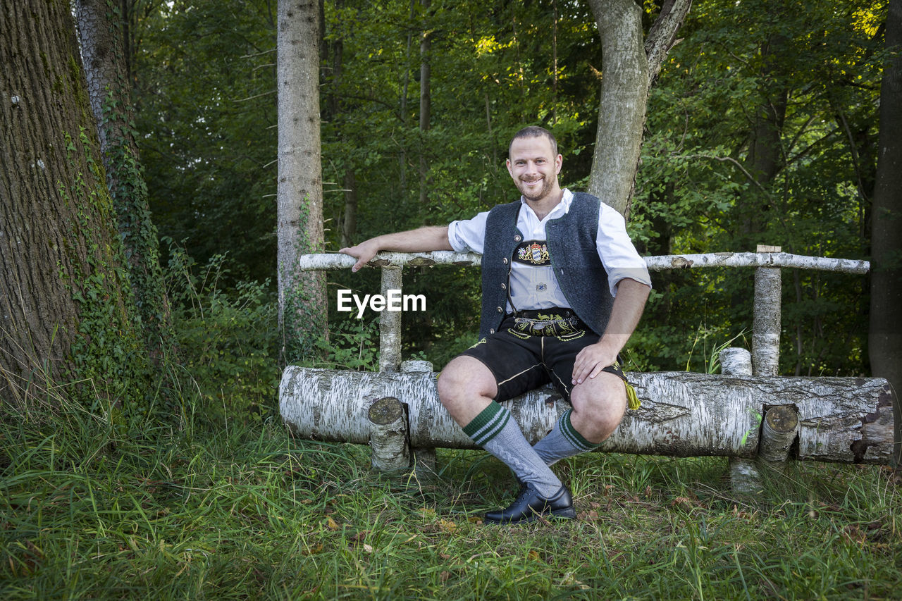 Portrait of smiling man sitting on seat in forest