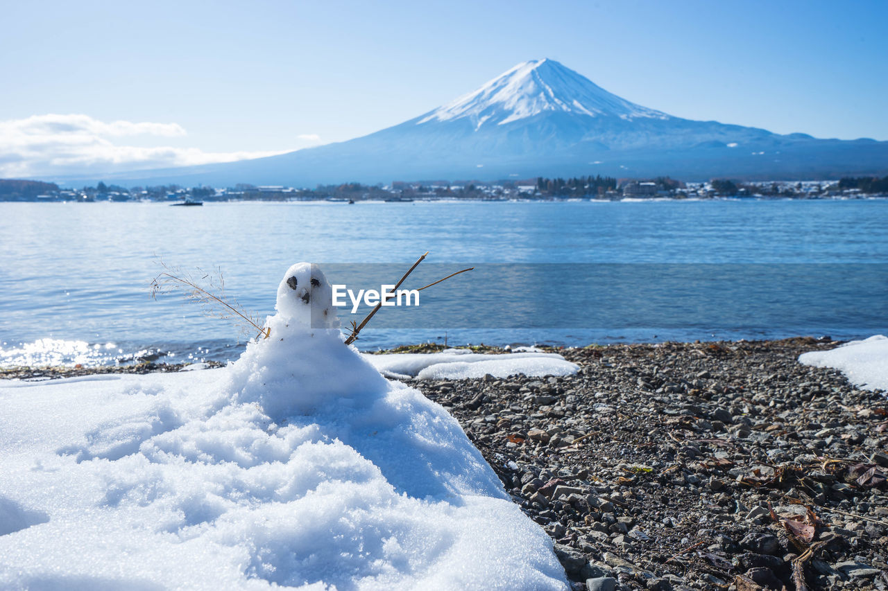 Snowman at lakeshore against snowcapped mountain