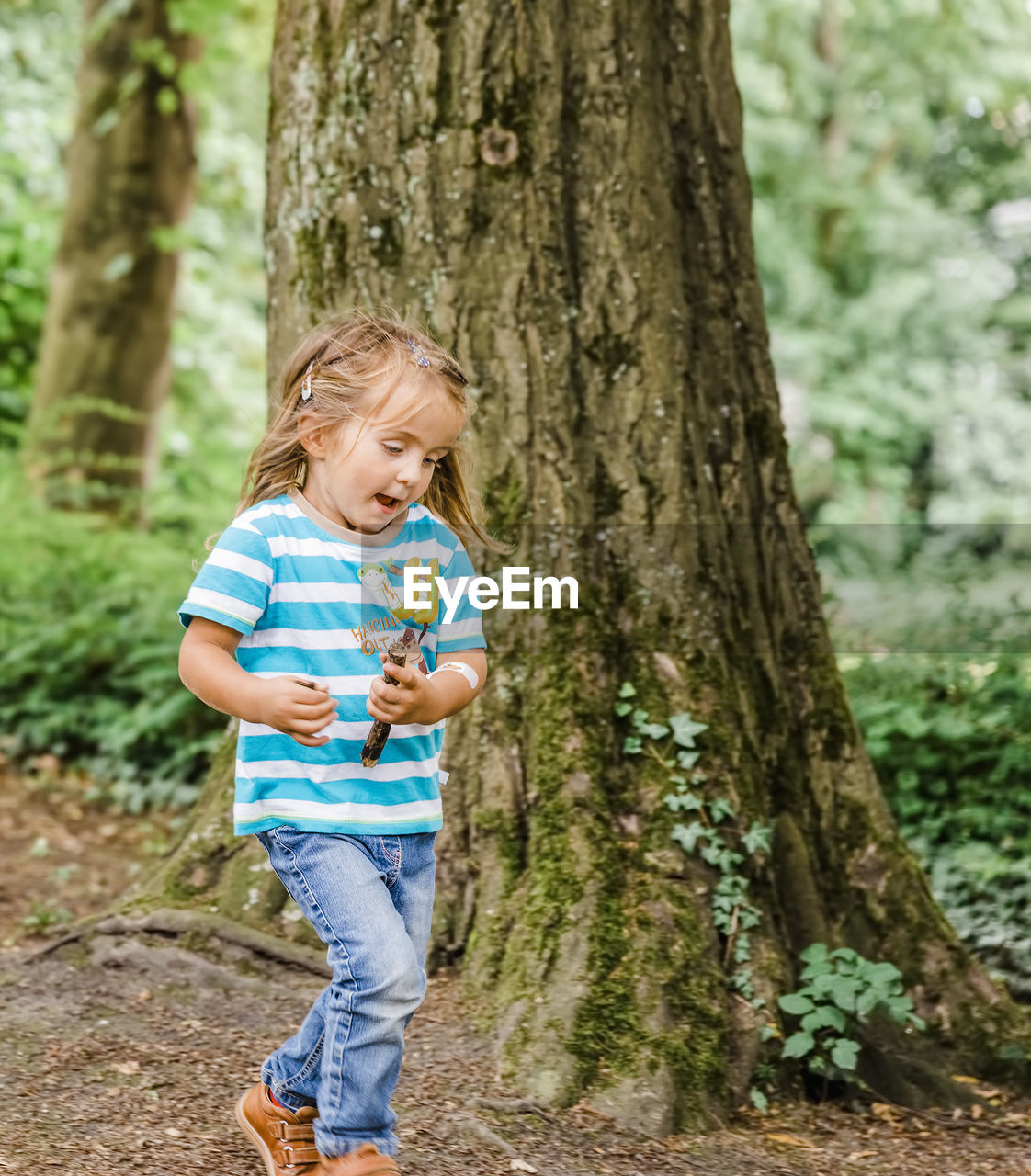 Girl walking by tree trunk in forest