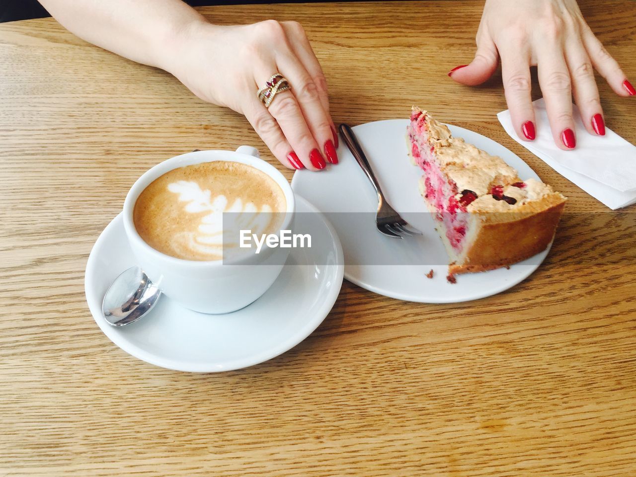 Cropped hands of woman with cake and coffee at wooden table